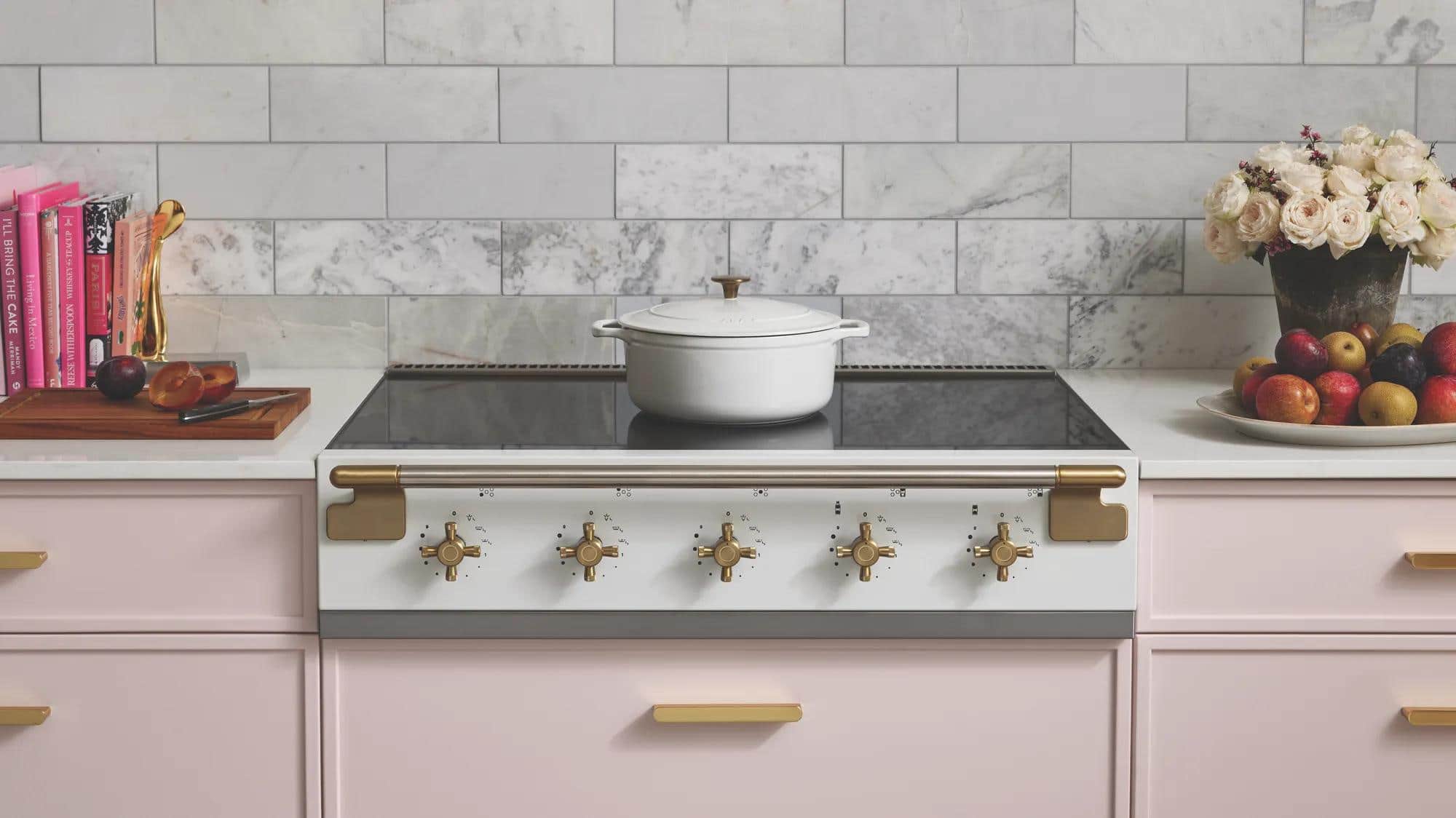A white AGA induction rangetop with brass controls in pale pink cabinetry
