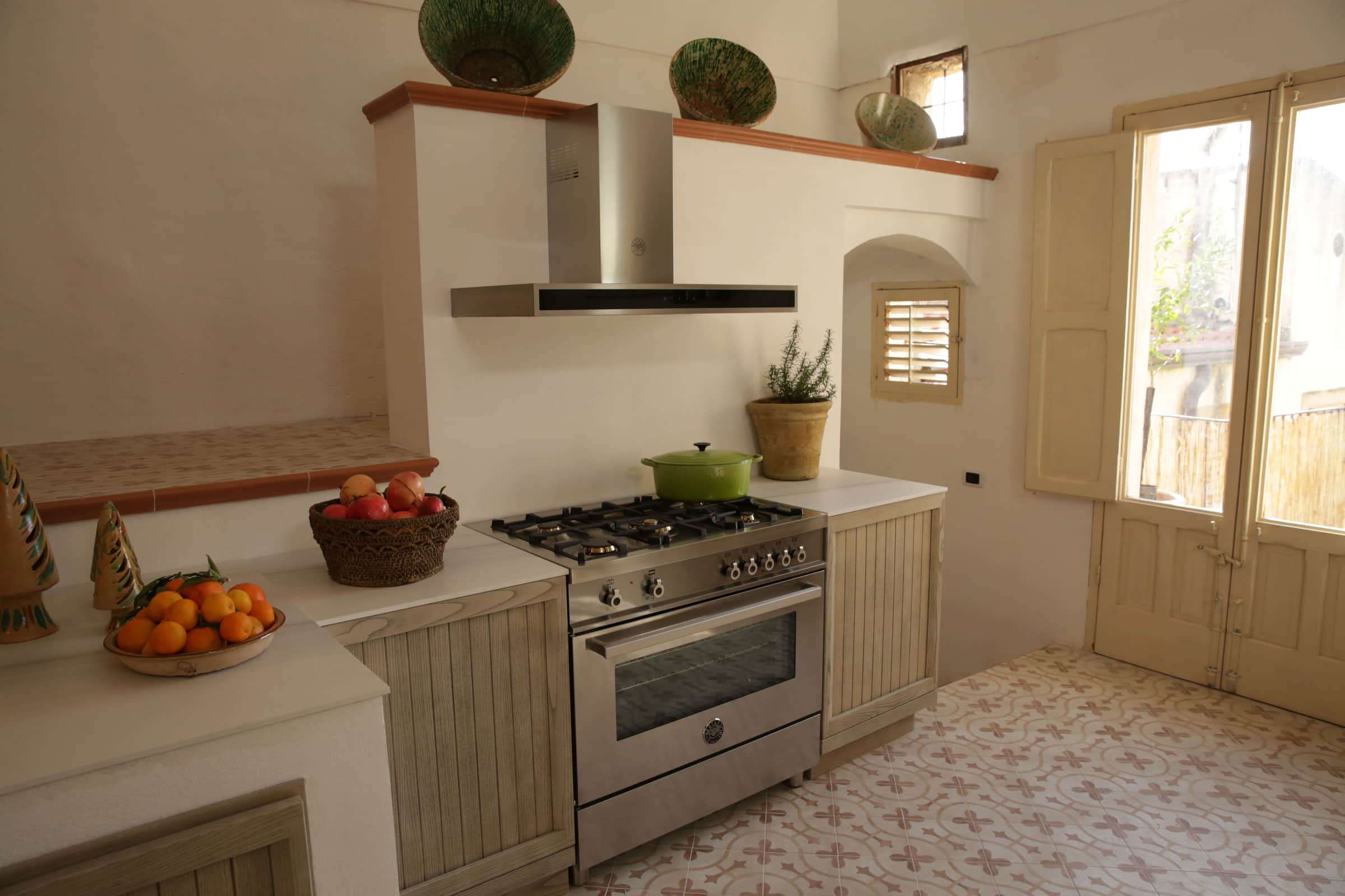 A stainless Bertazzoni range under a chimney hood in a rustic Italian kitchen with patterned terracotta tiles