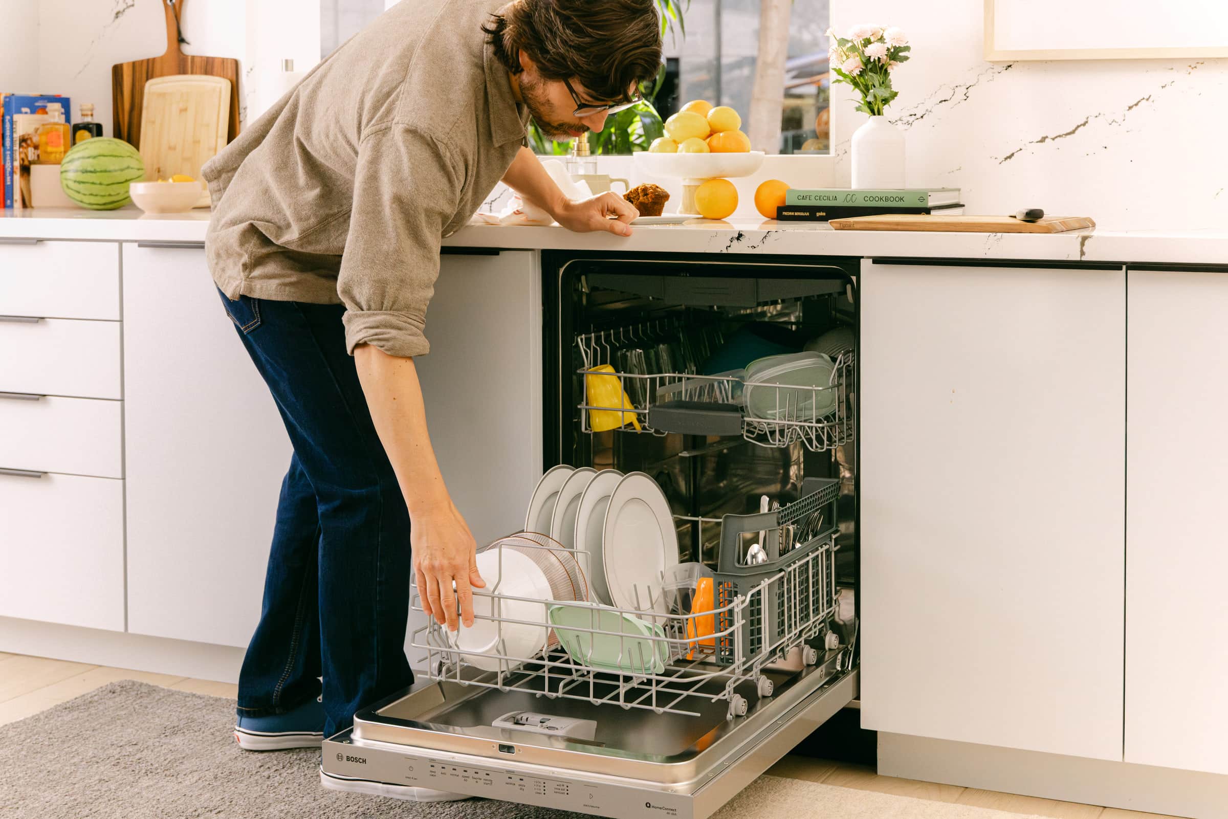A man loading plates into the lower rack of an open Bosch dishwasher