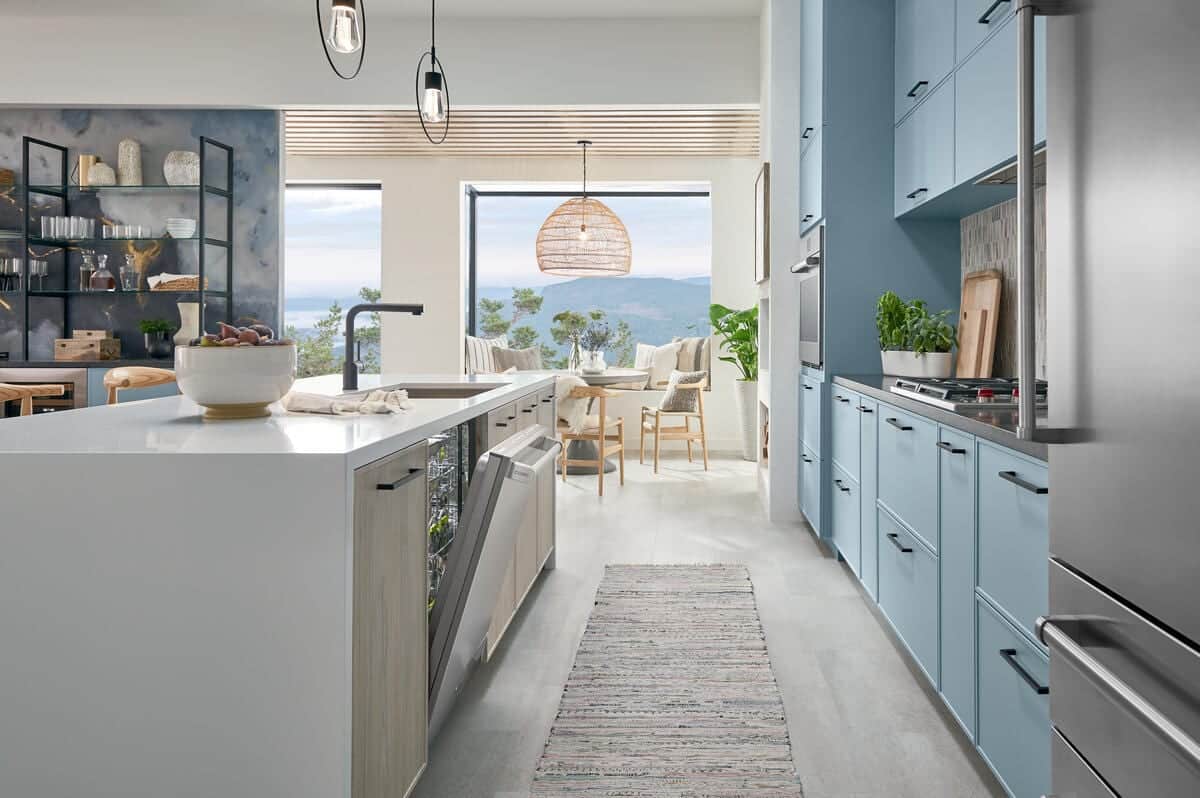 Galley view along a white quartz island housing a stainless Cove dishwasher, with blue cabinetry and a Wolf cooktop beyond