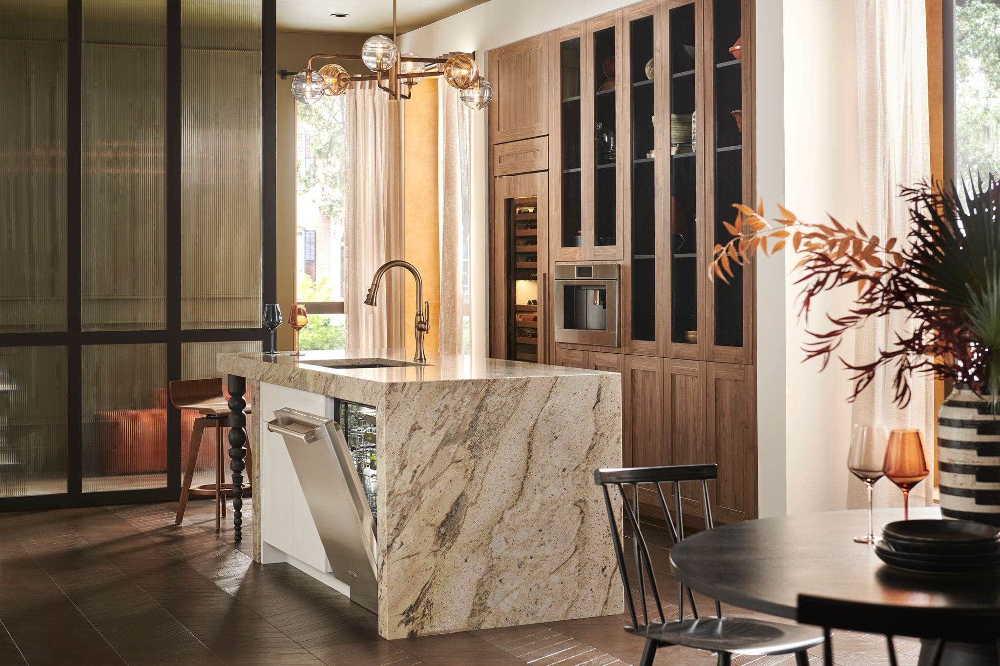 A Cove dishwasher set into a figured marble island beside walnut cabinetry
