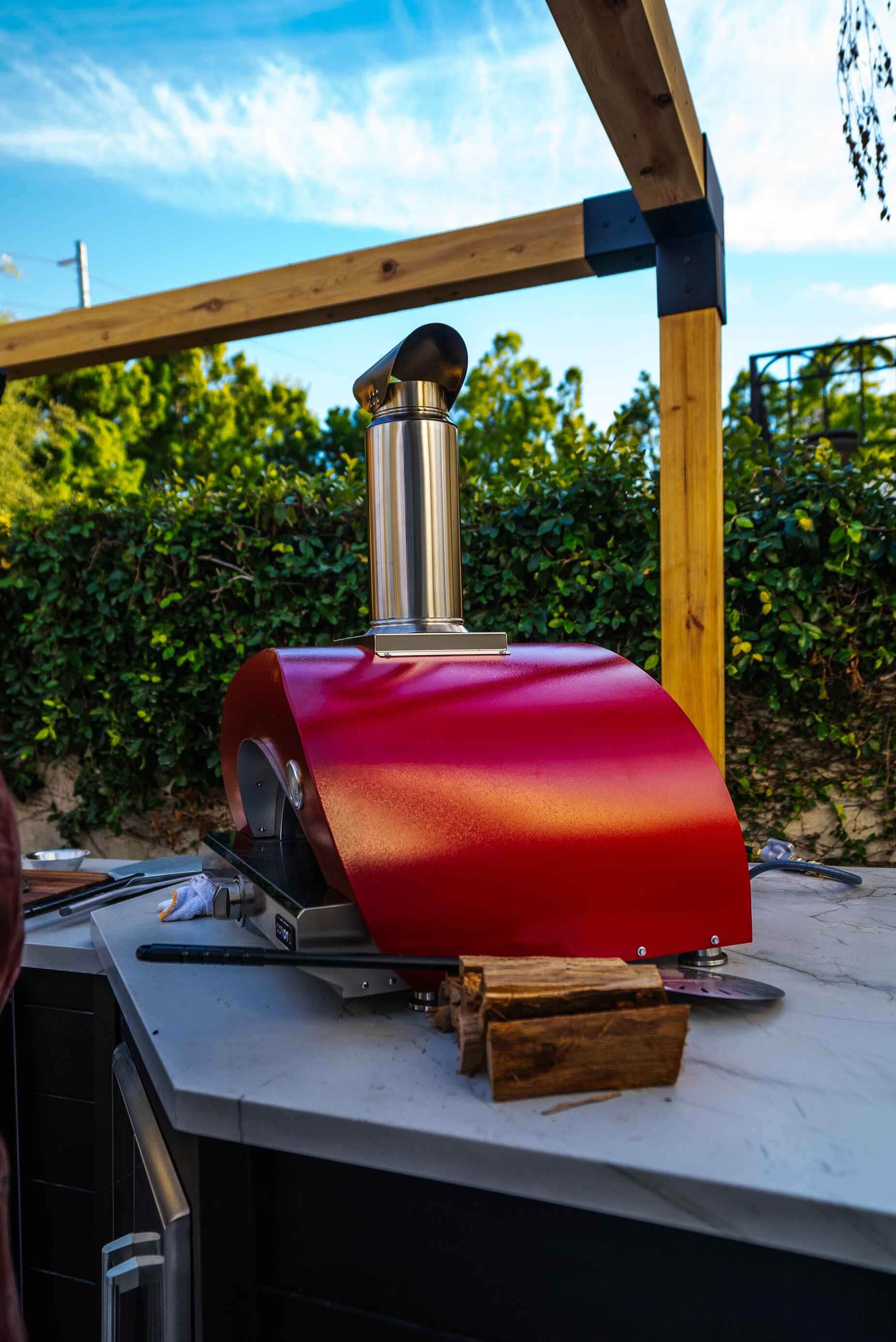 A red Coyote pizza oven on an outdoor counter under a pergola