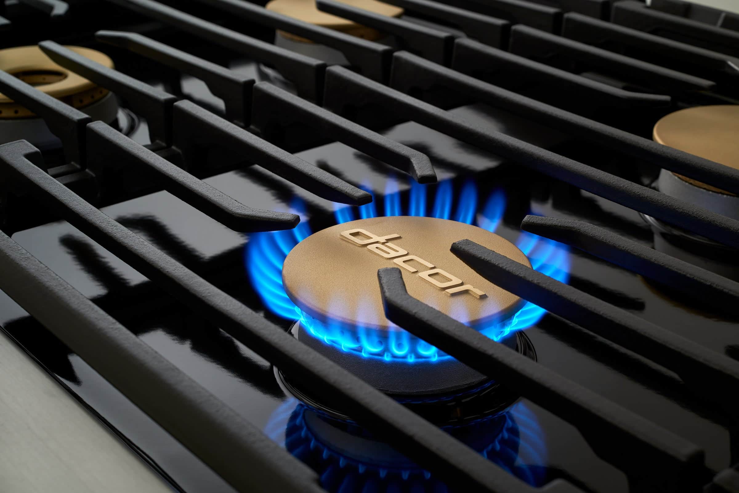 A brass Dacor burner cap under a ring of blue flame