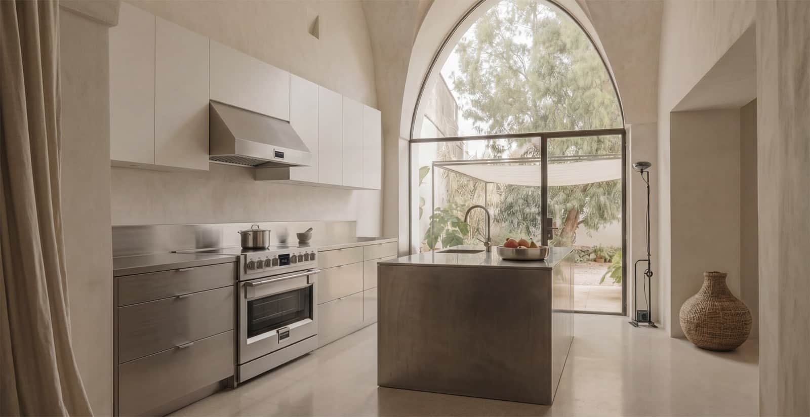 A stainless Fulgor Milano range in a minimal cream plaster kitchen with a stainless island and an arched garden window