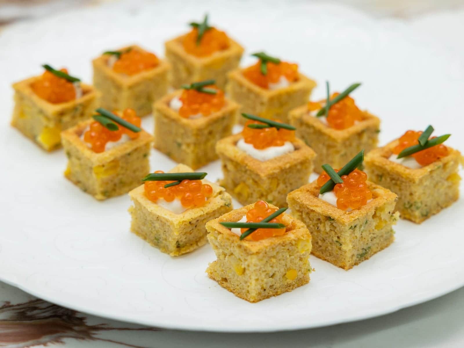 Cornbread canapes topped with salmon roe plated on a dark board