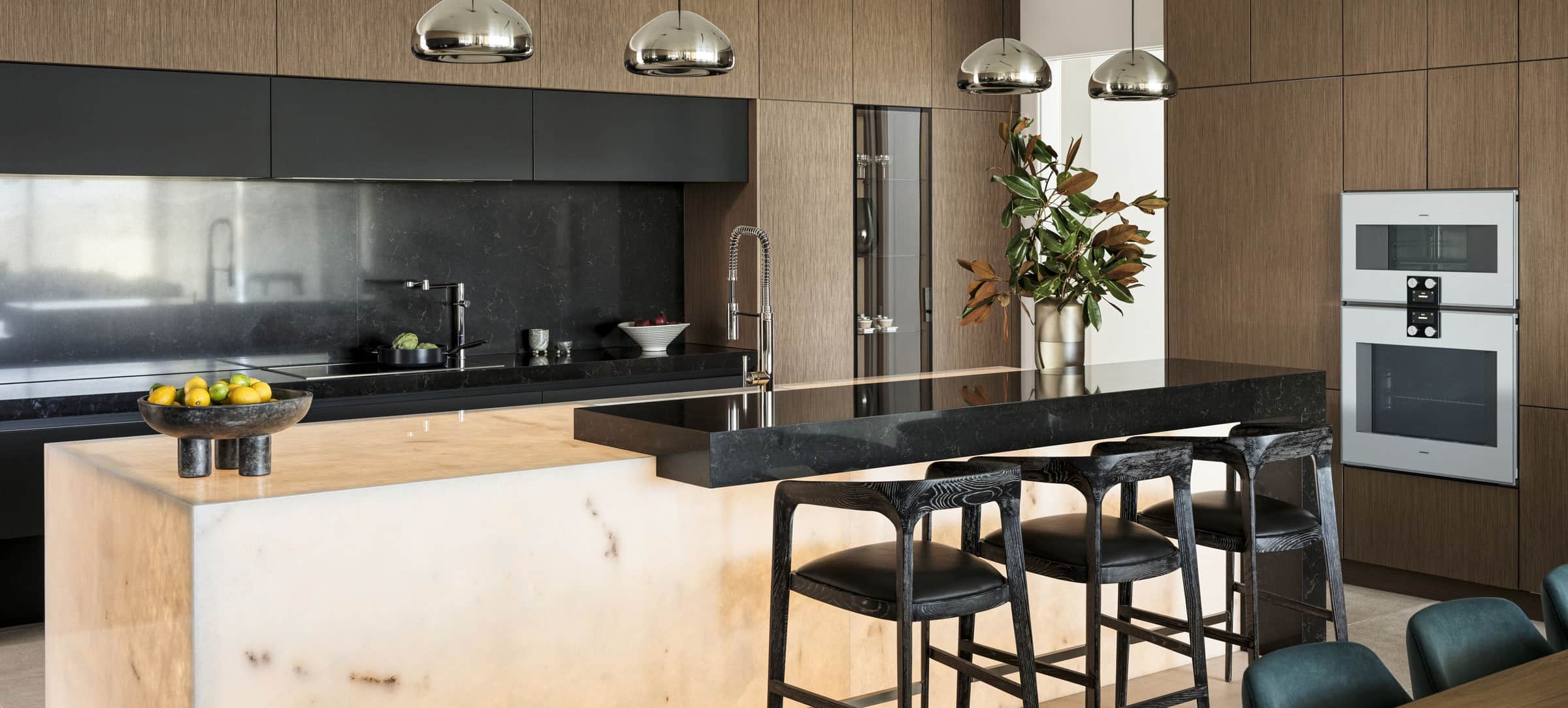 A dark kitchen with Gaggenau wall ovens and a backlit onyx island