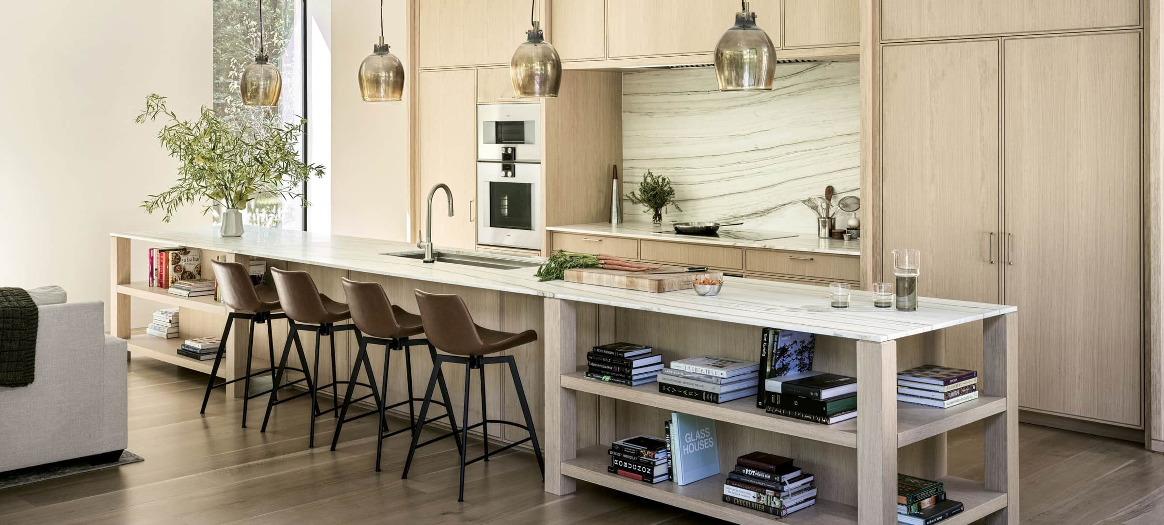An open-plan oak kitchen with Gaggenau wall ovens and a long marble island
