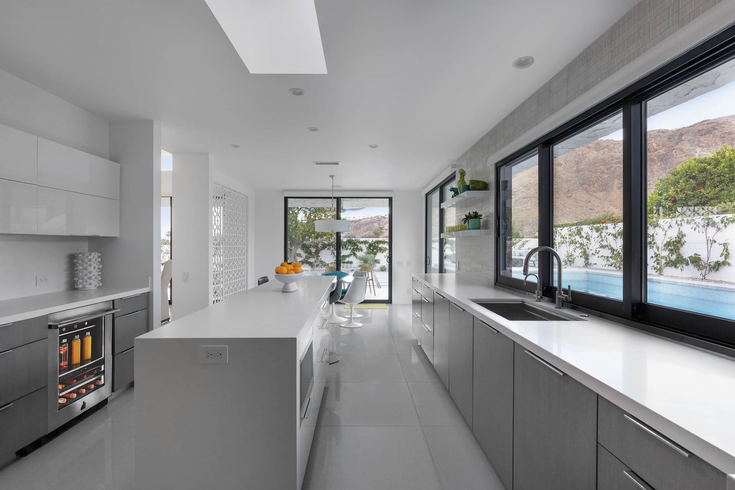 A JennAir beverage center in a white galley kitchen with a long island and a window wall