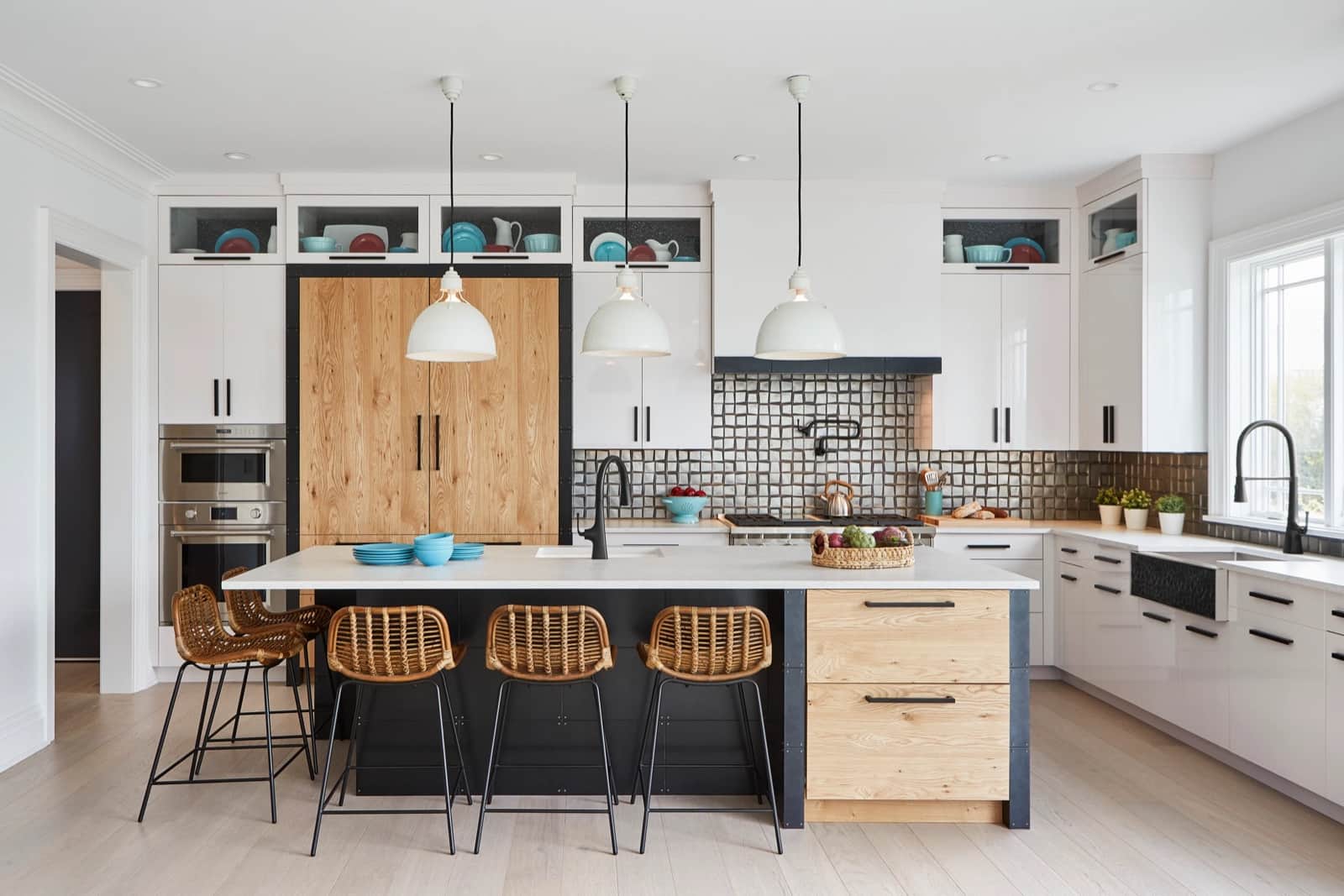 A white kitchen with a Kohler black kitchen faucet and apron-front sink, a marble island, and rattan counter stools