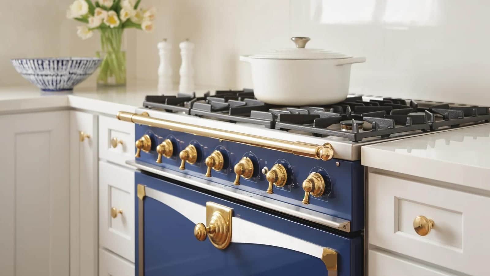 A blue La Cornue range with brass trim set into white cabinetry with a marble backsplash