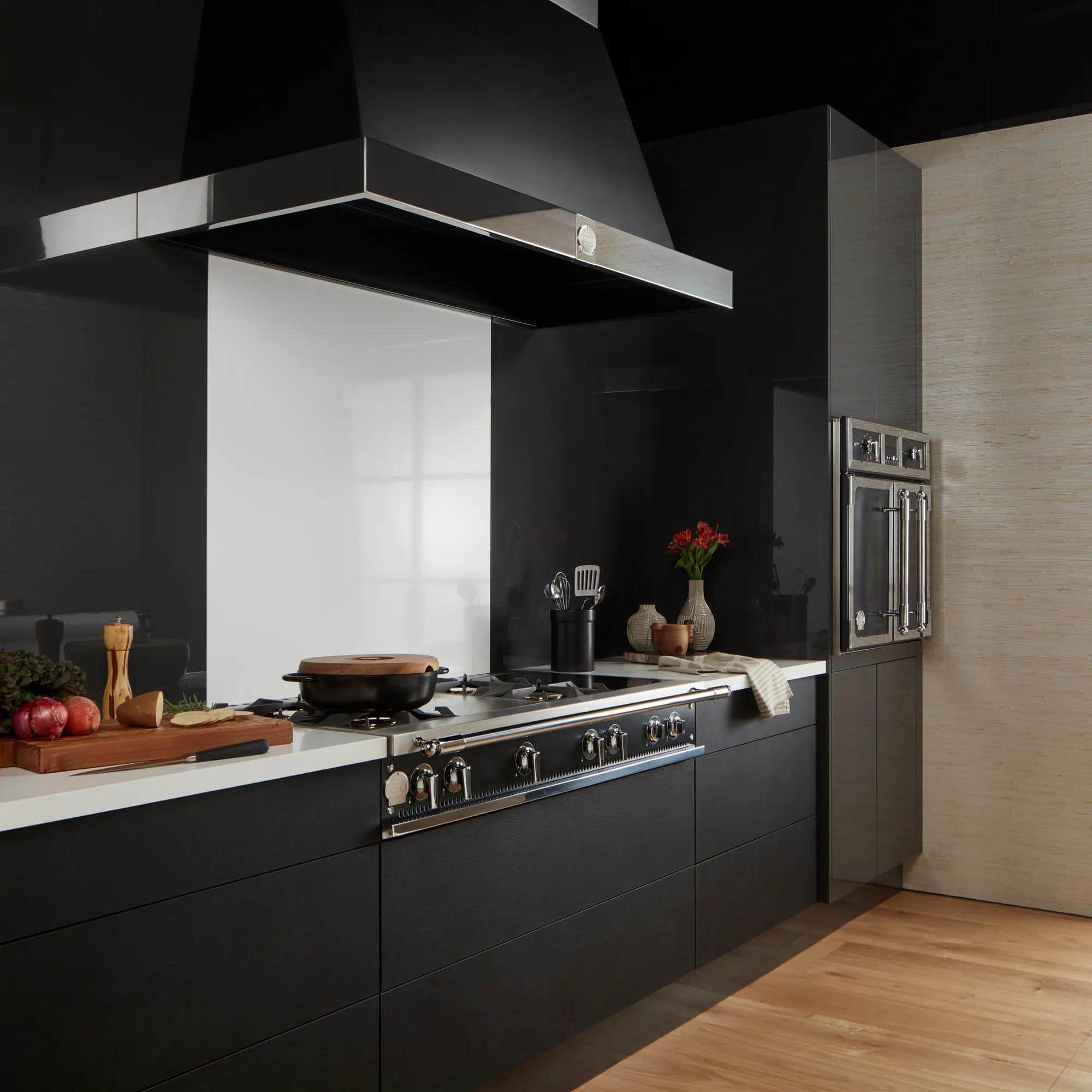 A stainless La Cornue cooktop and matching wall hood in a matte black kitchen with oak flooring and a built-in wall oven