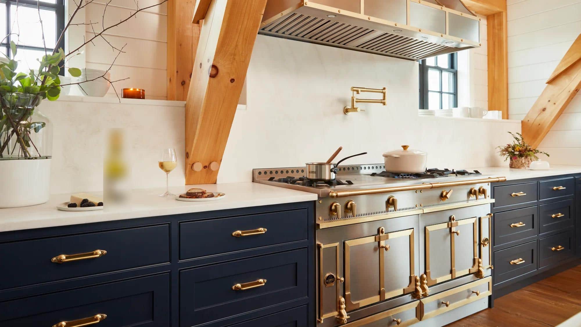 A stainless and brass La Cornue range between navy cabinets under timber beams