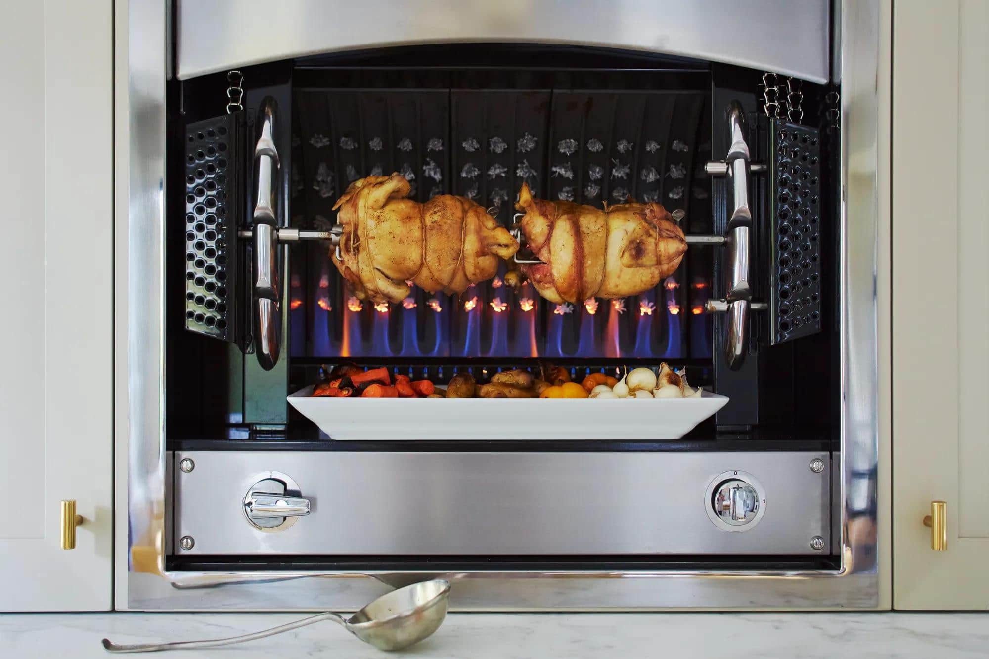 Two chickens turning over open flame in a La Cornue rotisserie