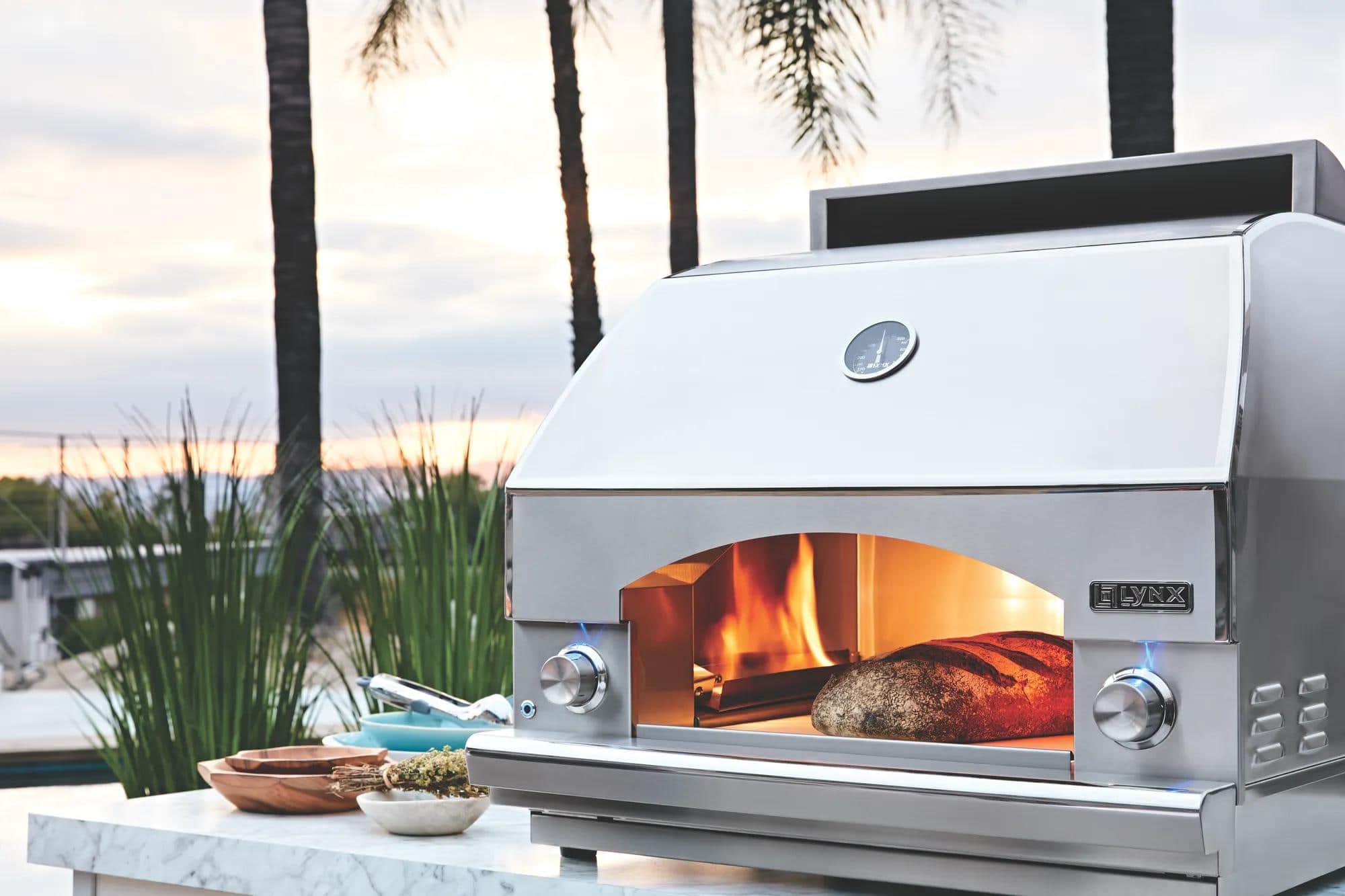 A Lynx outdoor pizza oven with a live fire and a loaf at the mouth