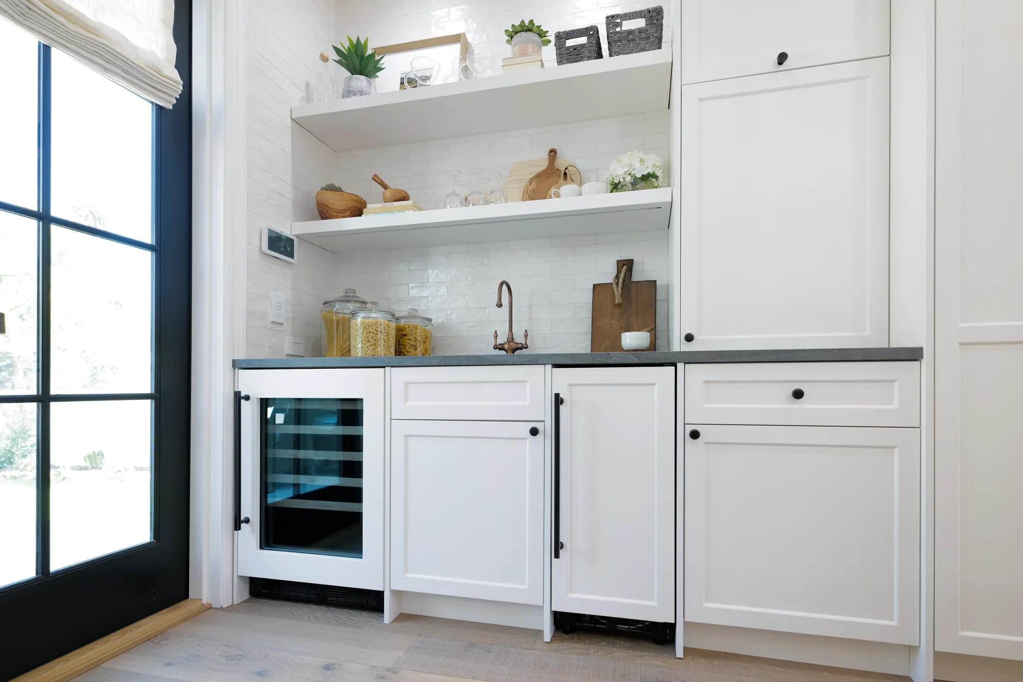A Marvel wine refrigerator built into a white kitchen nook beside a window