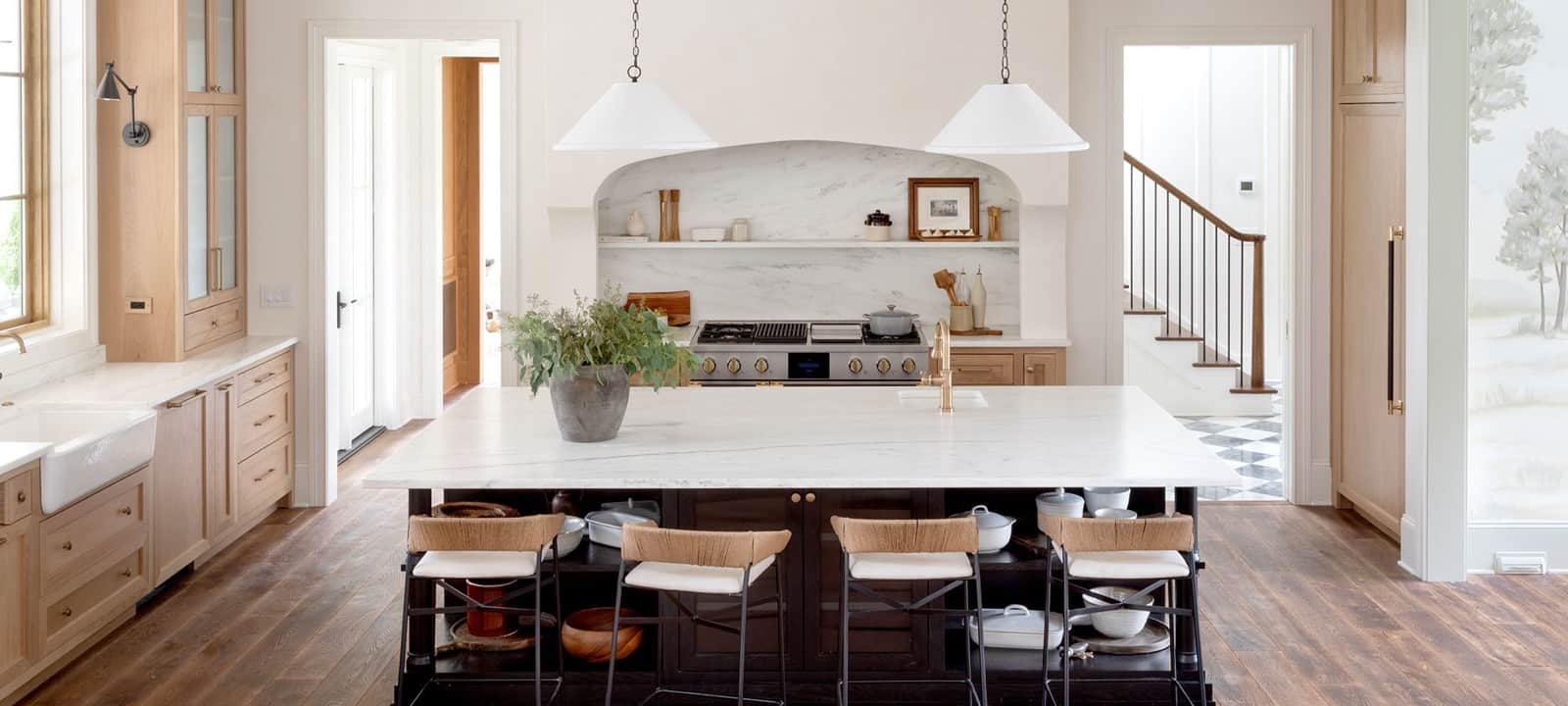 A stainless Monogram pro rangetop with brass knobs set into a marble alcove in a cream kitchen with a large marble island