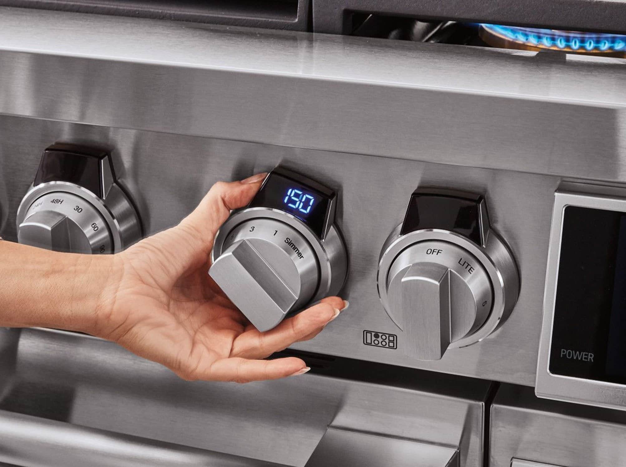 A hand turning a lit control knob on a stainless SKS range
