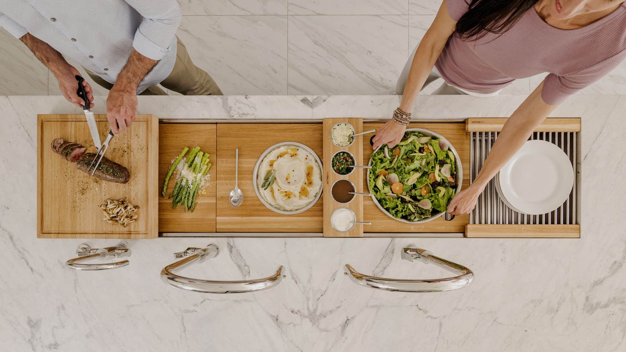 Two people serving from boards and bowls across a Galley workstation, seen from above