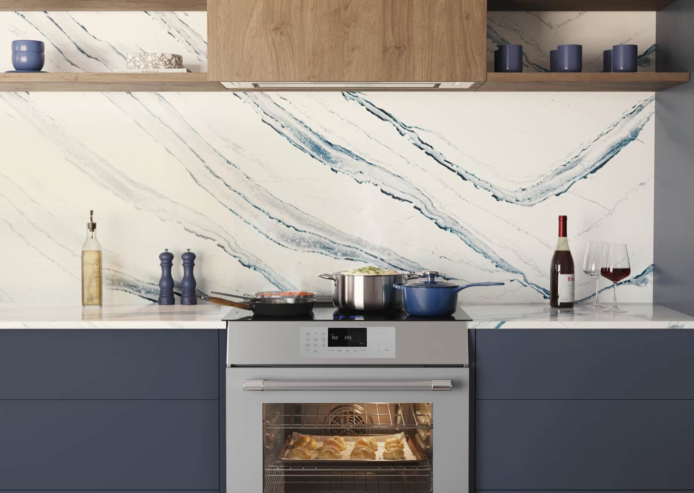 Front-on view of a Thermador range and wall hood in a navy kitchen with a large blue-veined marble slab backsplash and pastries baking in the open oven