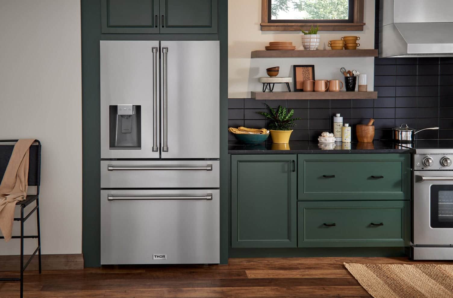 A stainless Thor Kitchen French-door refrigerator with a water dispenser, built into dark green cabinetry beside open wood shelves and a black tile backsplash