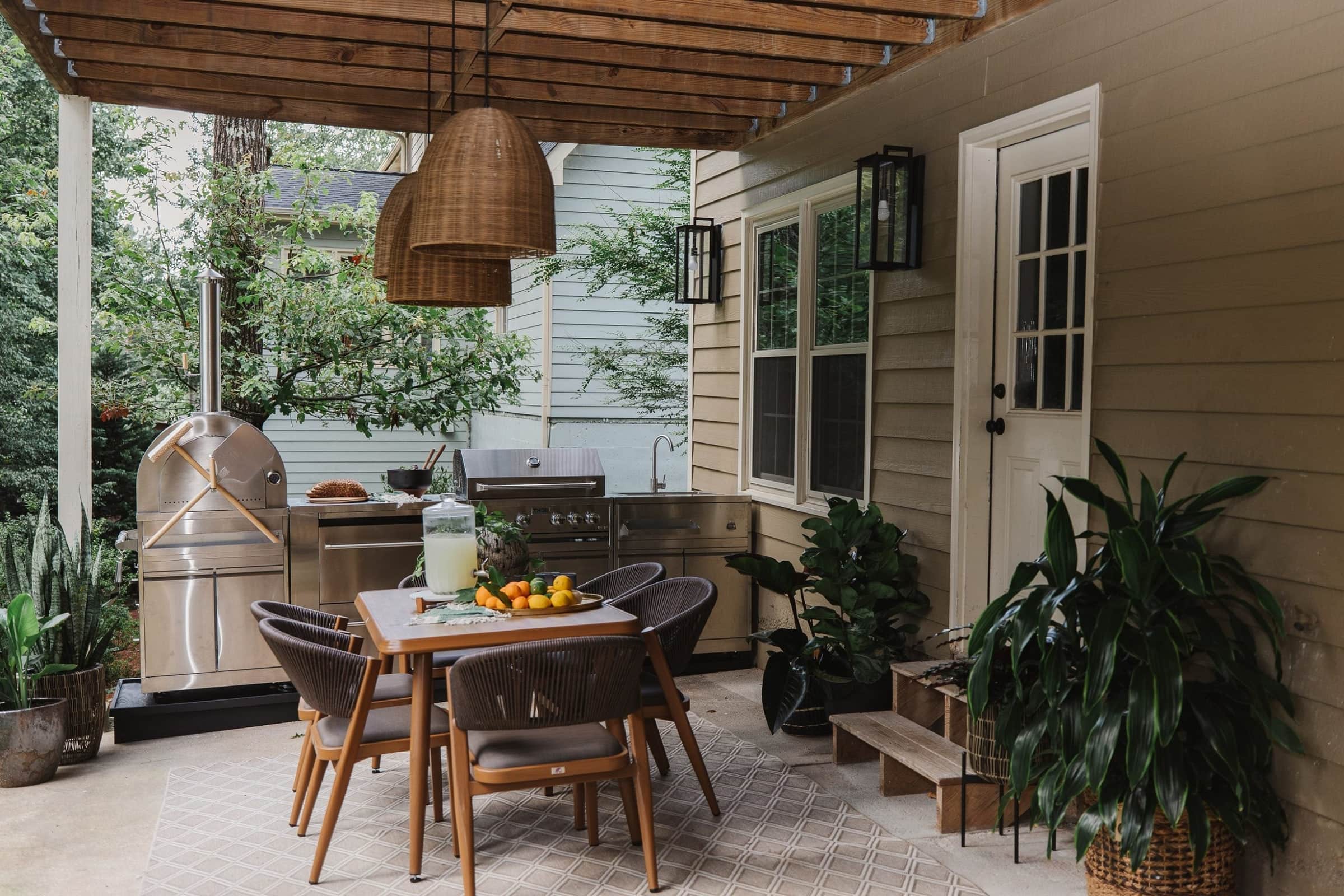 A covered patio with a Thor Kitchen outdoor grill and pizza oven behind a dining table