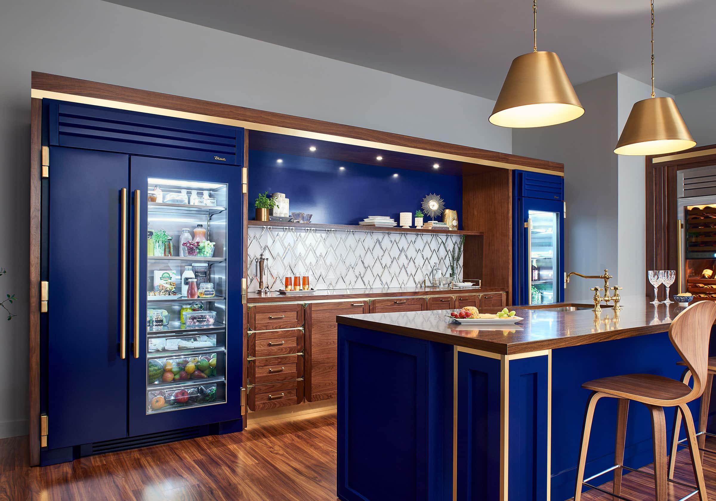 Cobalt True Residential glass-door refrigerator columns framed in walnut beside a blue island
