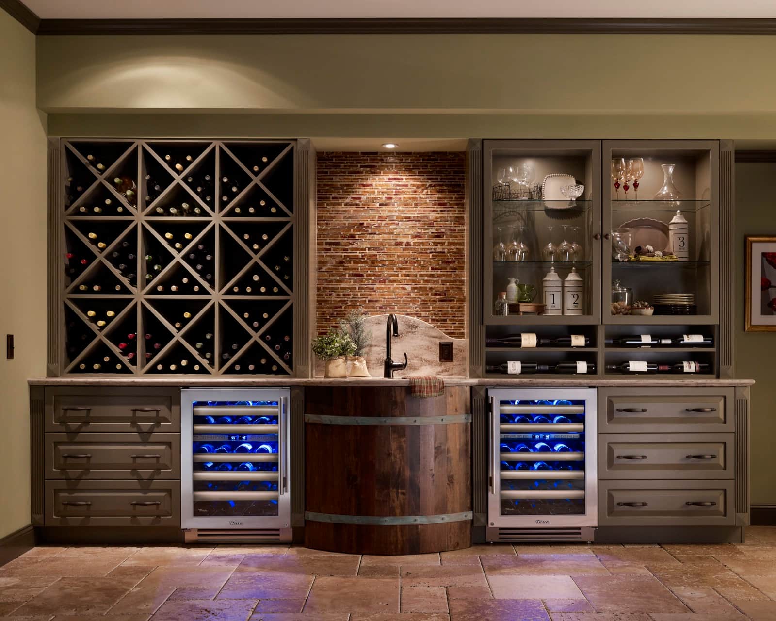 Two stainless glass-door True Residential dual-zone wine cabinets lit blue, flanking a wine-barrel sink base in a taupe wet bar