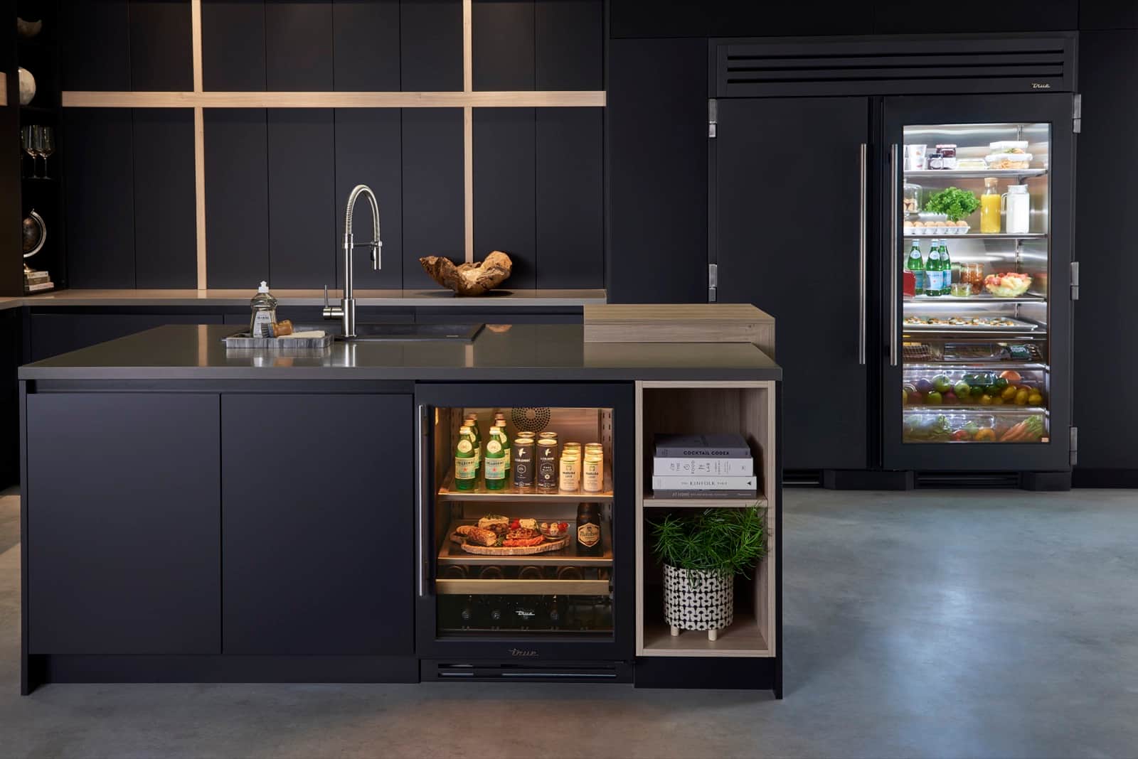 Matte black kitchen with an open glass-door True Residential undercounter beverage cabinet and a black glass-door refrigerator column behind