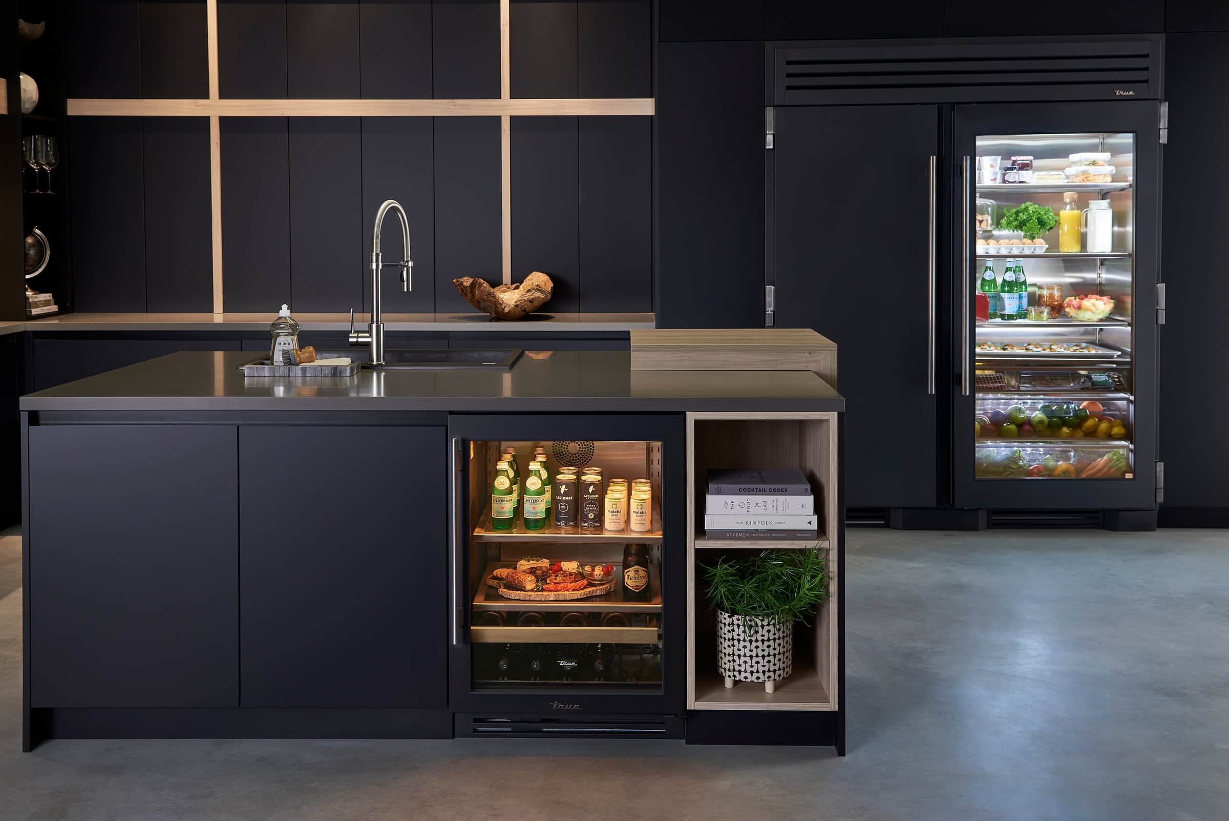 Matte black kitchen with an open glass-door True Residential undercounter beverage cabinet and a black glass-door refrigerator column behind