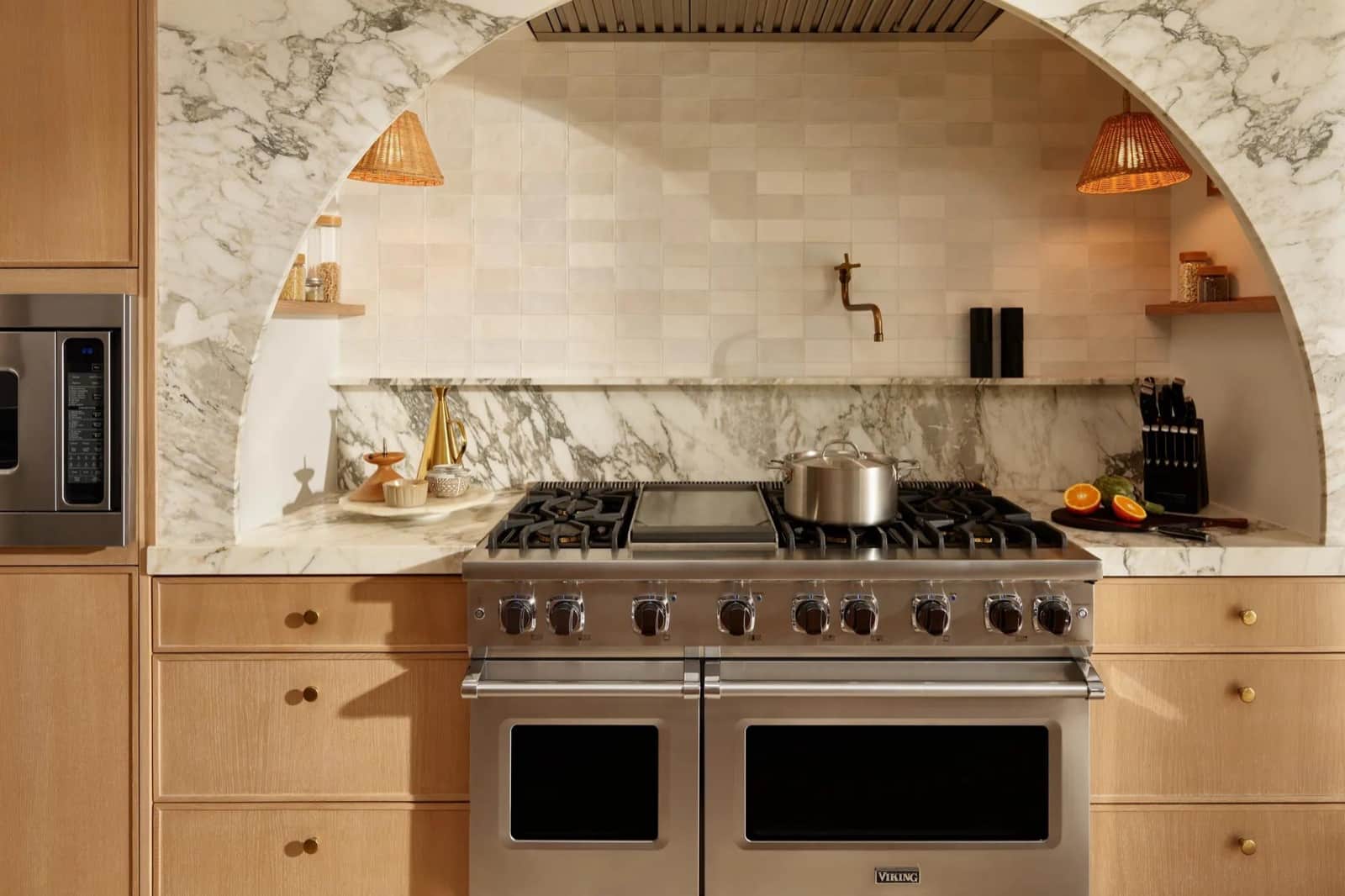 A stainless 48-inch Viking range with a center griddle set into an arched marble alcove with zellige tile in an oak kitchen