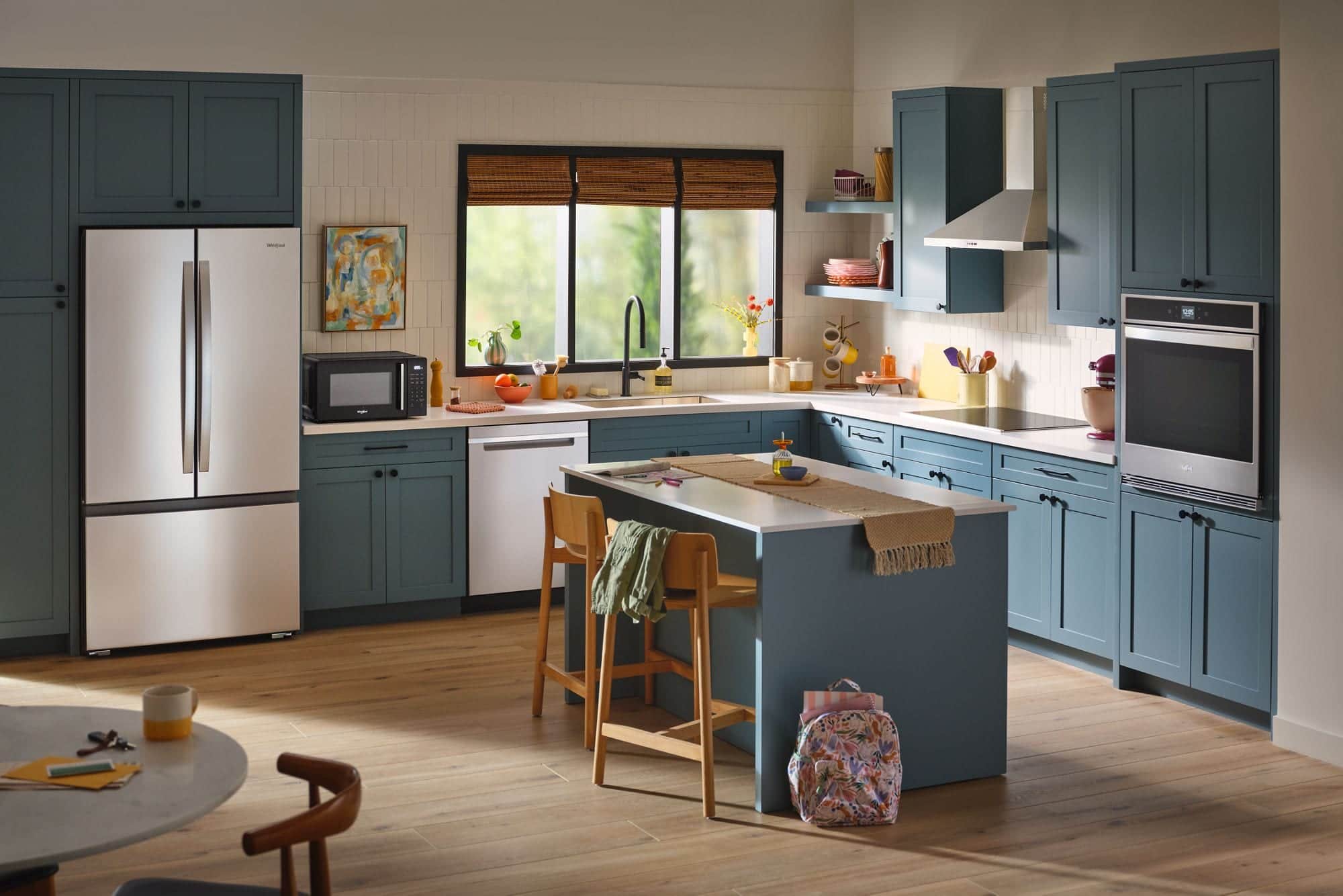 A stainless Whirlpool French-door refrigerator, a black countertop microwave and a stainless wall oven in a kitchen with dark teal cabinets and an island