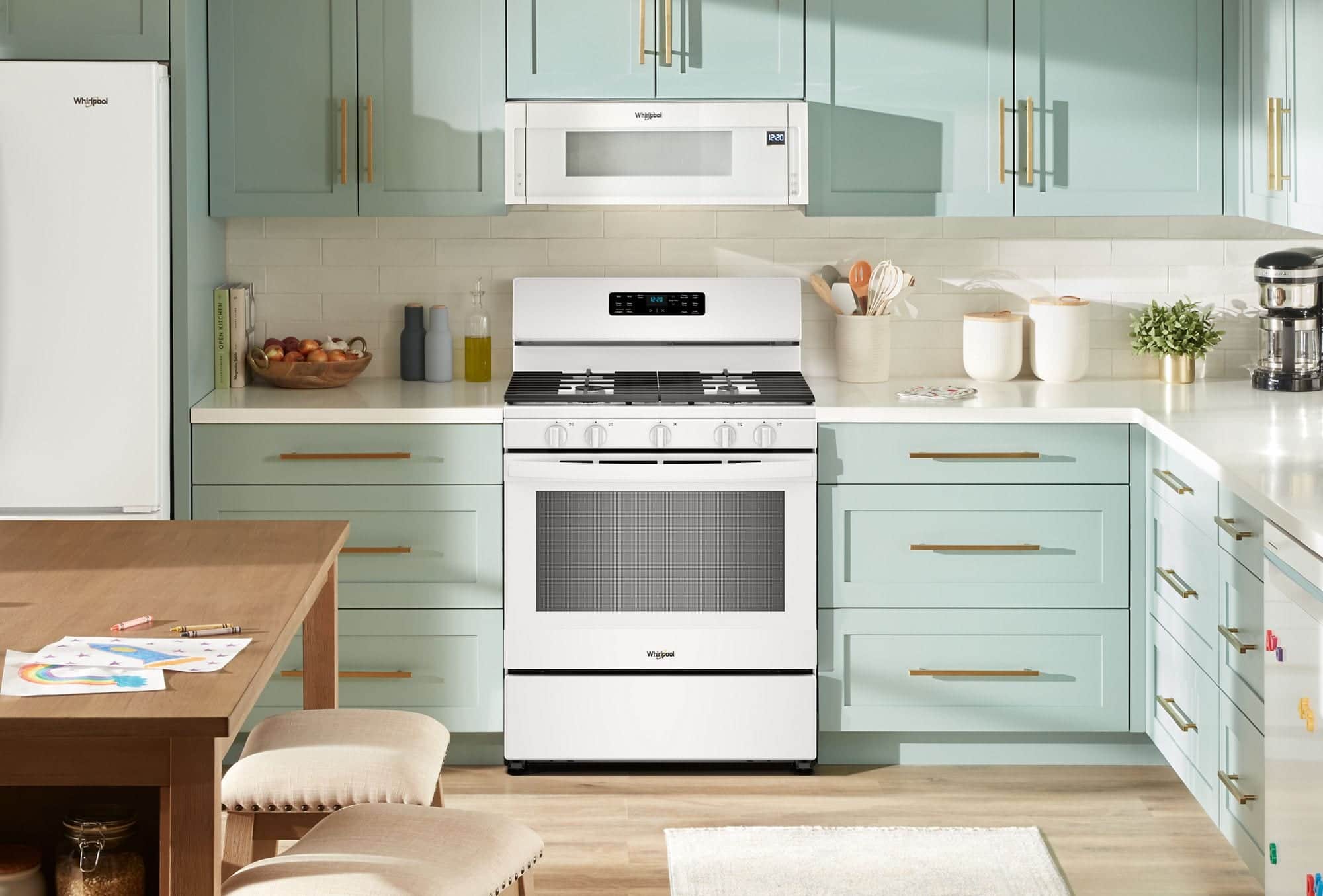 A white Whirlpool gas range under a white low-profile microwave, a white refrigerator at the left, in a kitchen with mint green cabinets