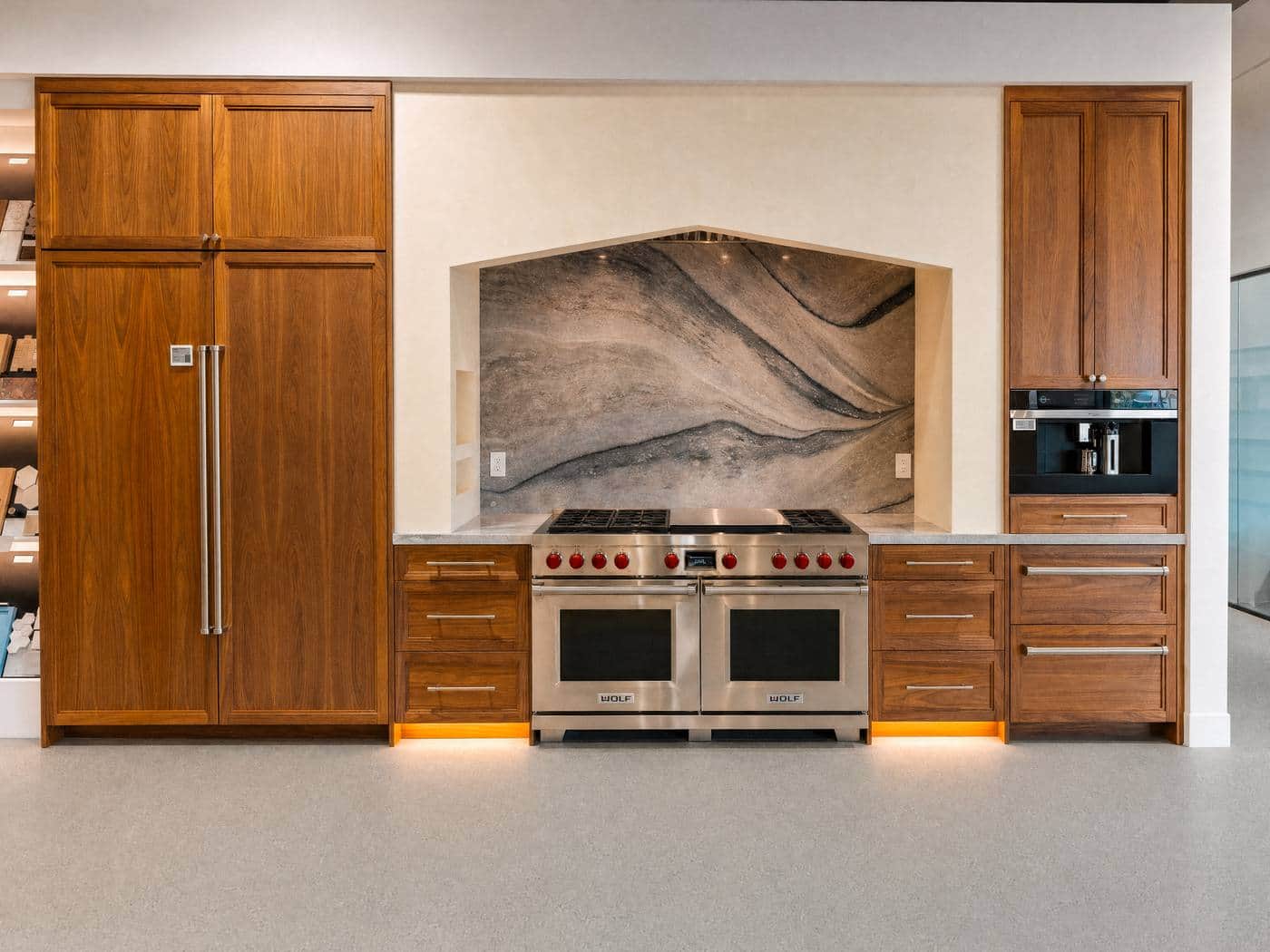 Wolf stainless double range with red knobs beneath a stone alcove, walnut cabinetry either side