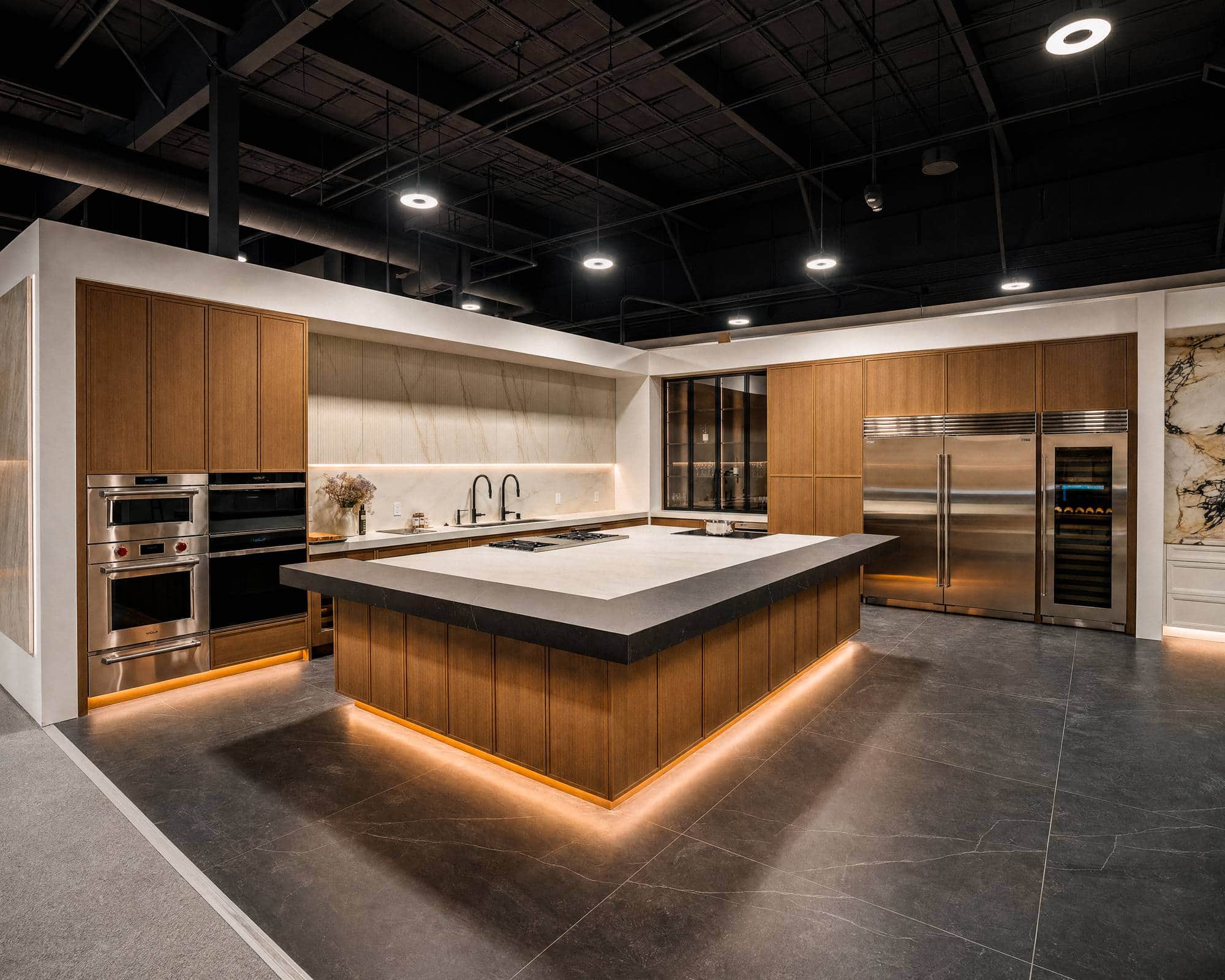 The Roseville showroom floor: wall ovens at left, stainless refrigerator and wine columns at right, a lit island between