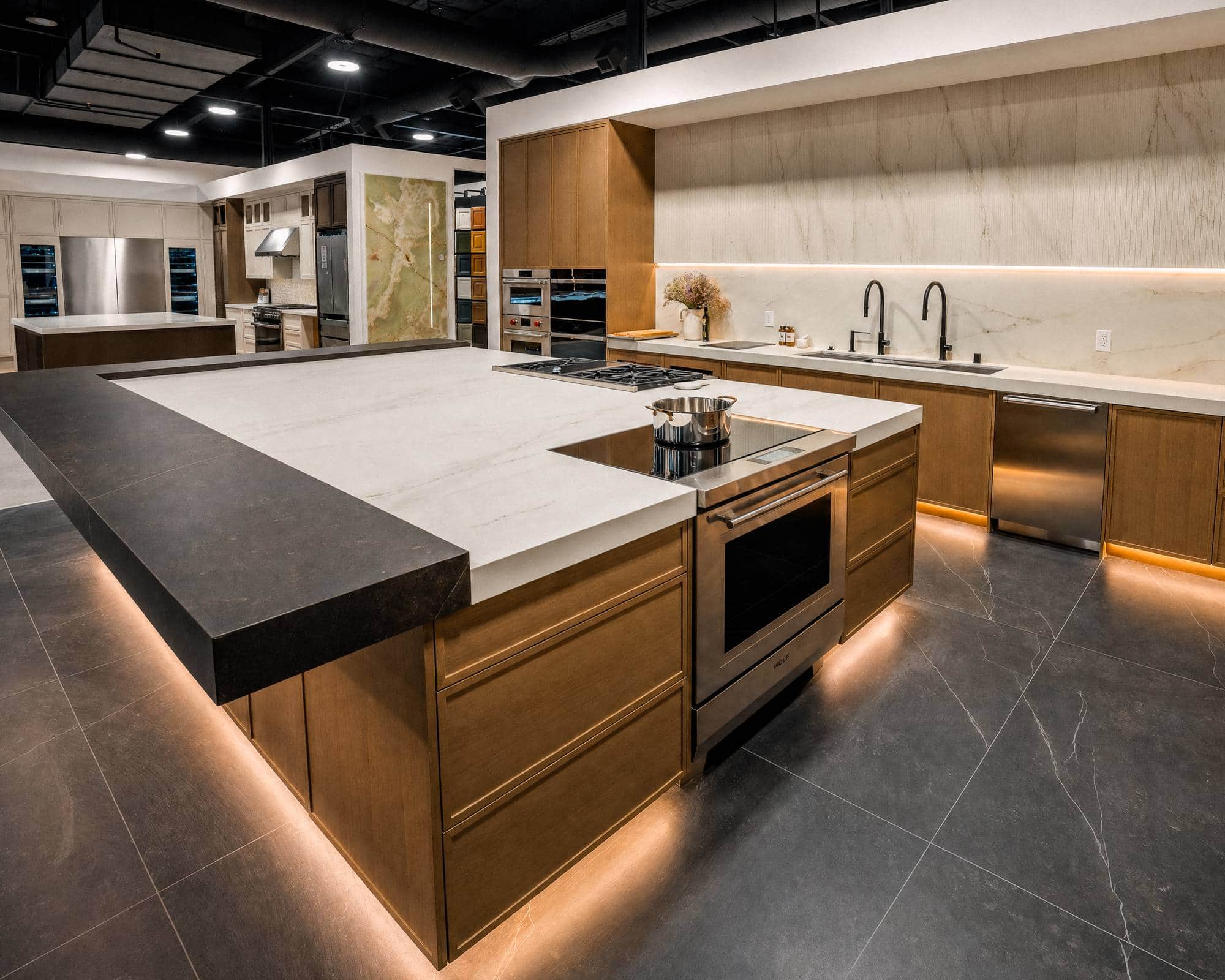 A wide view of the showroom floor: an island range and cooktop, a materials display and refrigerator columns beyond