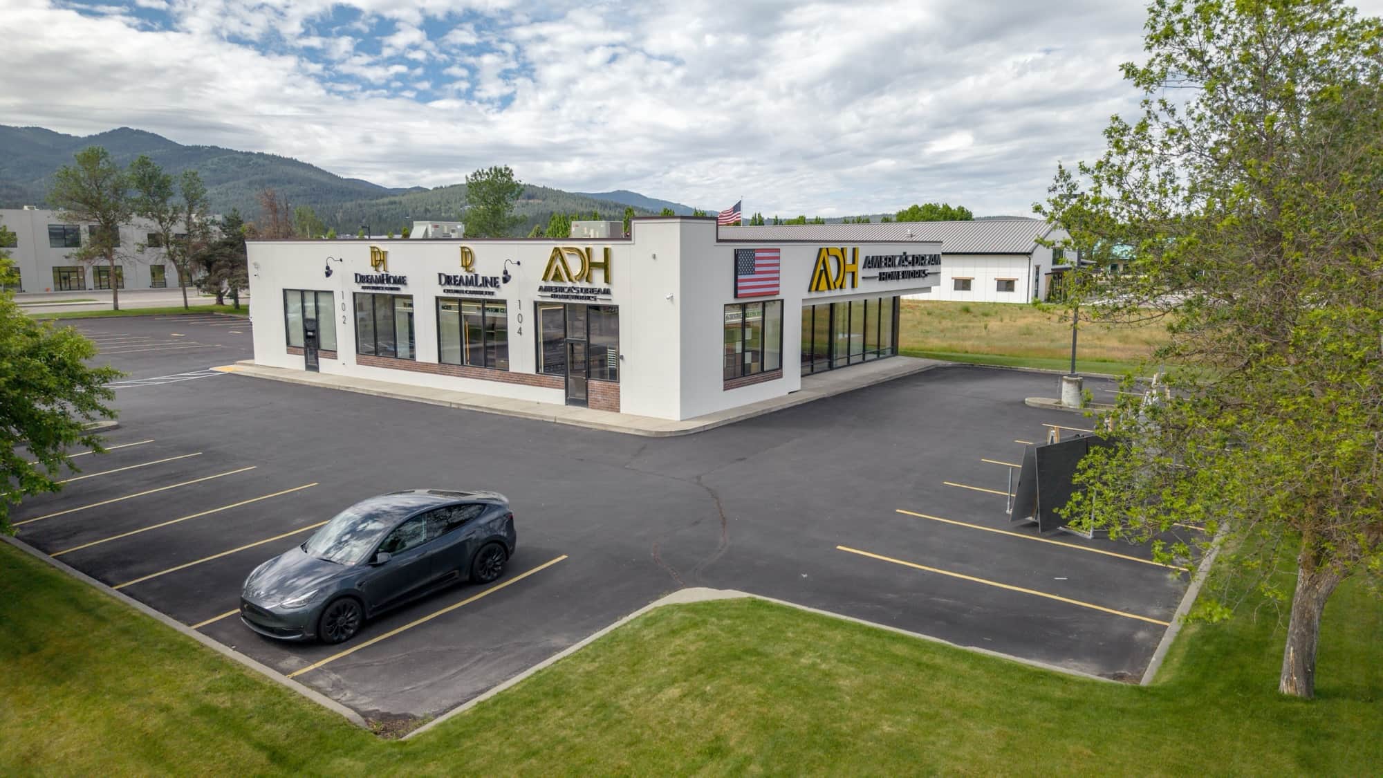 The single-story showroom building at 104 S Moyie St in Post Falls seen across its parking lot, with glass suite entrances along the front elevation and forested hills behind
