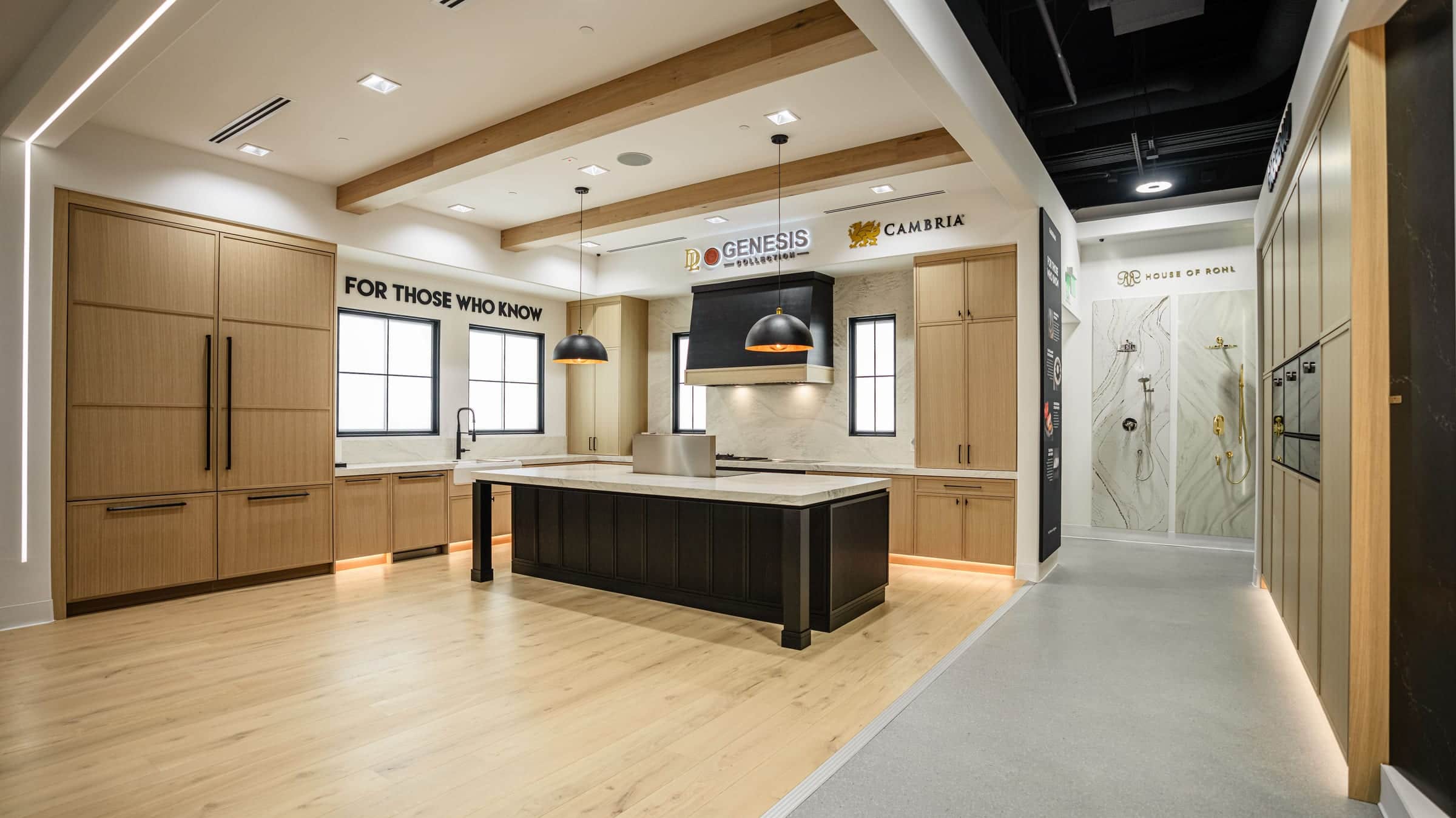 An oak display kitchen with a black island and a black hood beside the main aisle of the Roseville showroom, with a shower display further down the walkway
