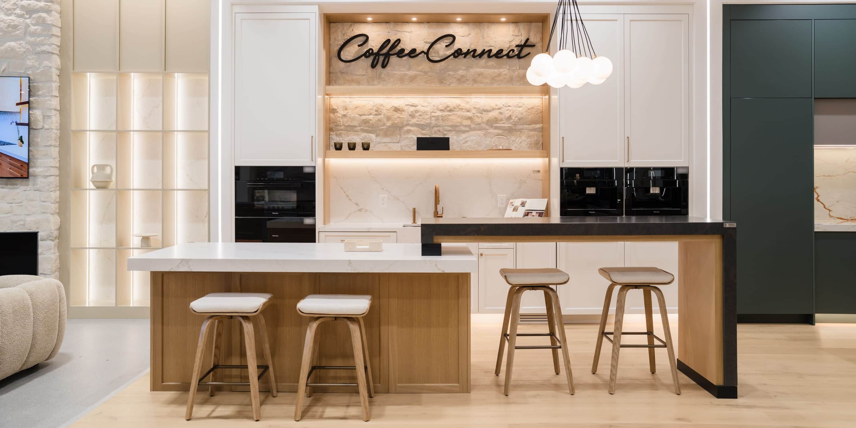 A coffee station display in the Roseville showroom: two built-in coffee systems in white cabinetry, a stone-clad shelf and a two-level island with bar stools