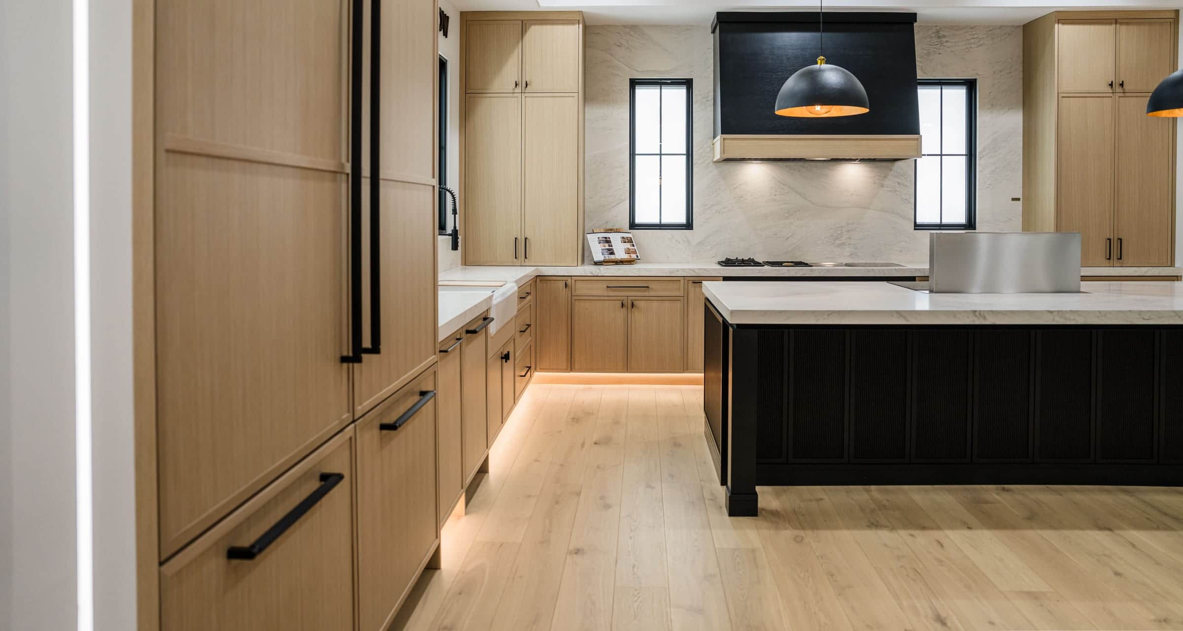 Panel-ready refrigeration columns behind rift oak panels with long black pulls, leading to a black island and a black hood in a Roseville showroom display