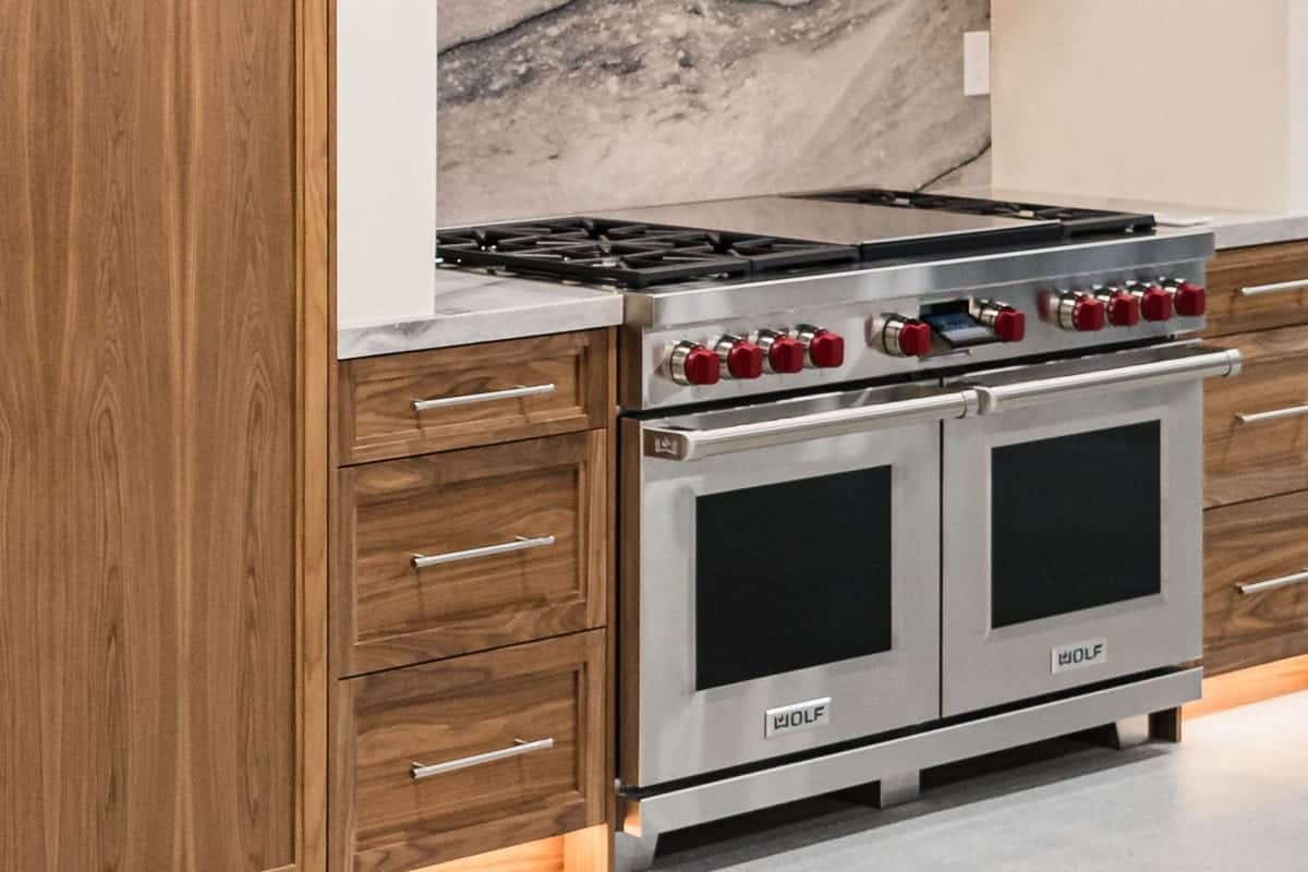 A dual-fuel range with red control knobs and a griddle between walnut drawer stacks in the Roseville showroom, a veined stone backsplash behind it