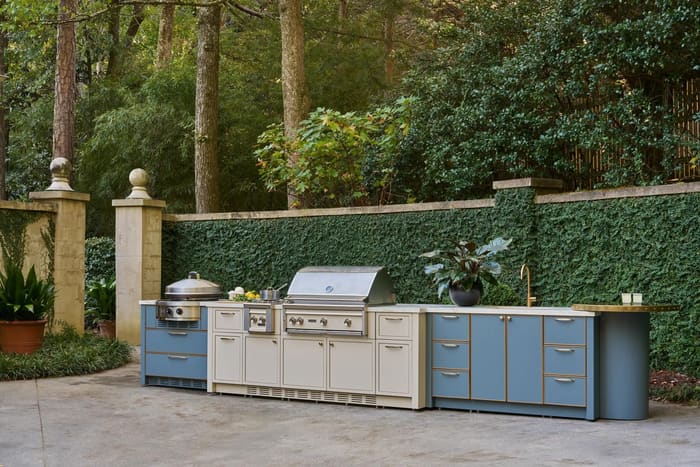 A Lynx outdoor kitchen with a stainless built-in grill, side burner, and blue cabinetry set along a garden wall