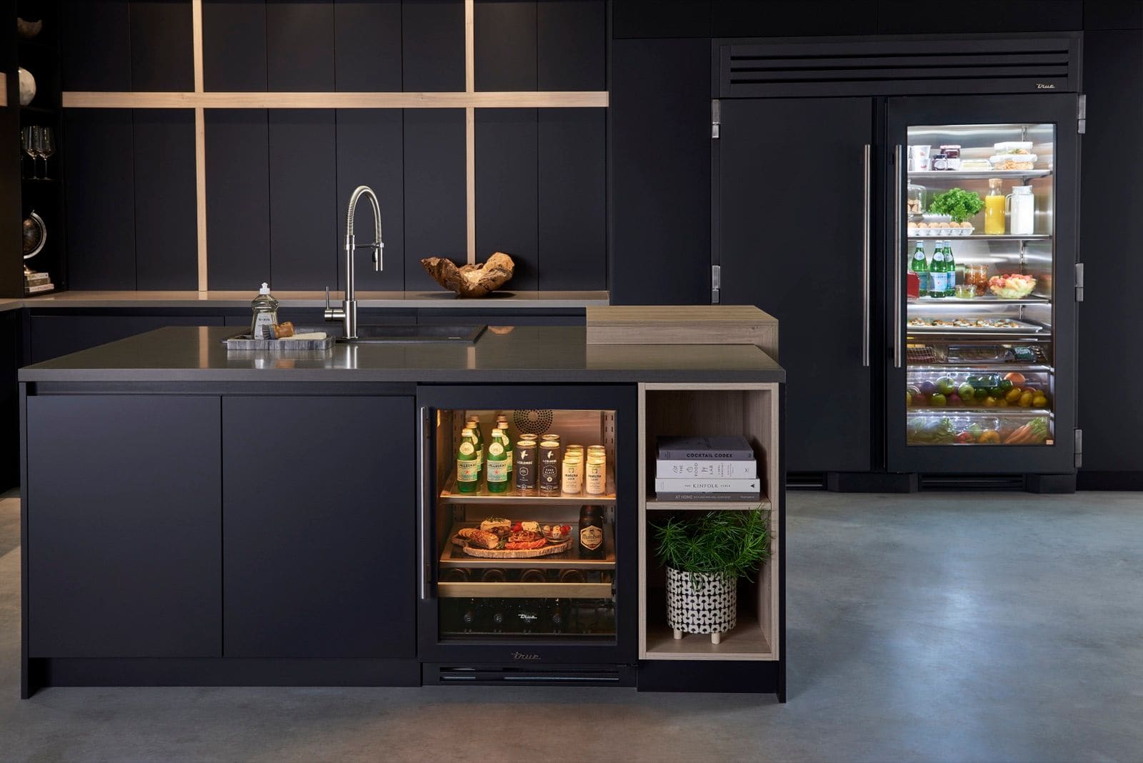 Matte black kitchen with an open glass-door True Residential undercounter beverage cabinet and a black glass-door refrigerator column behind