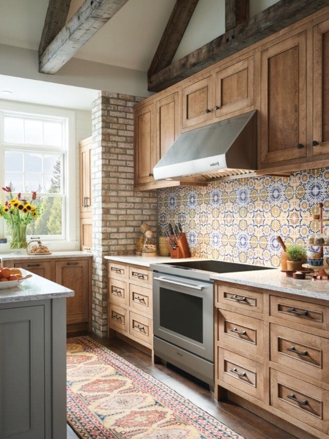 Stainless Wolf range and matching wall hood set against a blue and yellow patterned tile backsplash in a rustic oak kitchen